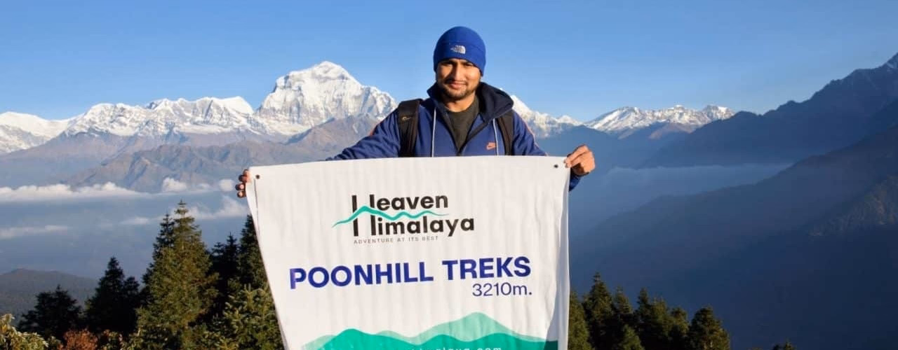 Ramhari Adhikari holding a "Poonhill Treks" banner in front of the snow-capped Annapurna mountains