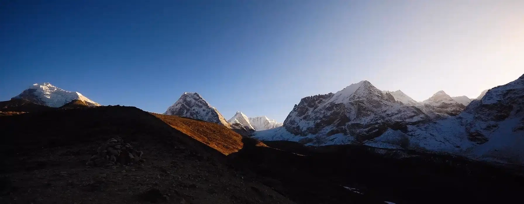 A dramatic view of snow-capped Himalayan peaks rising above the rugged valley trails of the Everest region