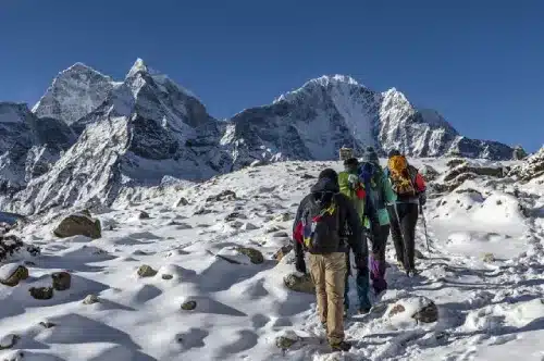 Four trekkers walking on snow towards the base camp of Mt Everest with other highest peaks in the background.
