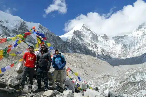 Travelers posing for a photo in the Everest Base Camp near the Khumbu glacier with high mountains standing tall in the background.